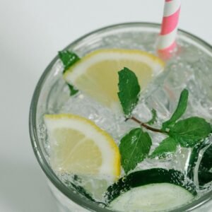 Close-up of a refreshing drink with lemon slices, mint leaves, and a pastel striped straw.