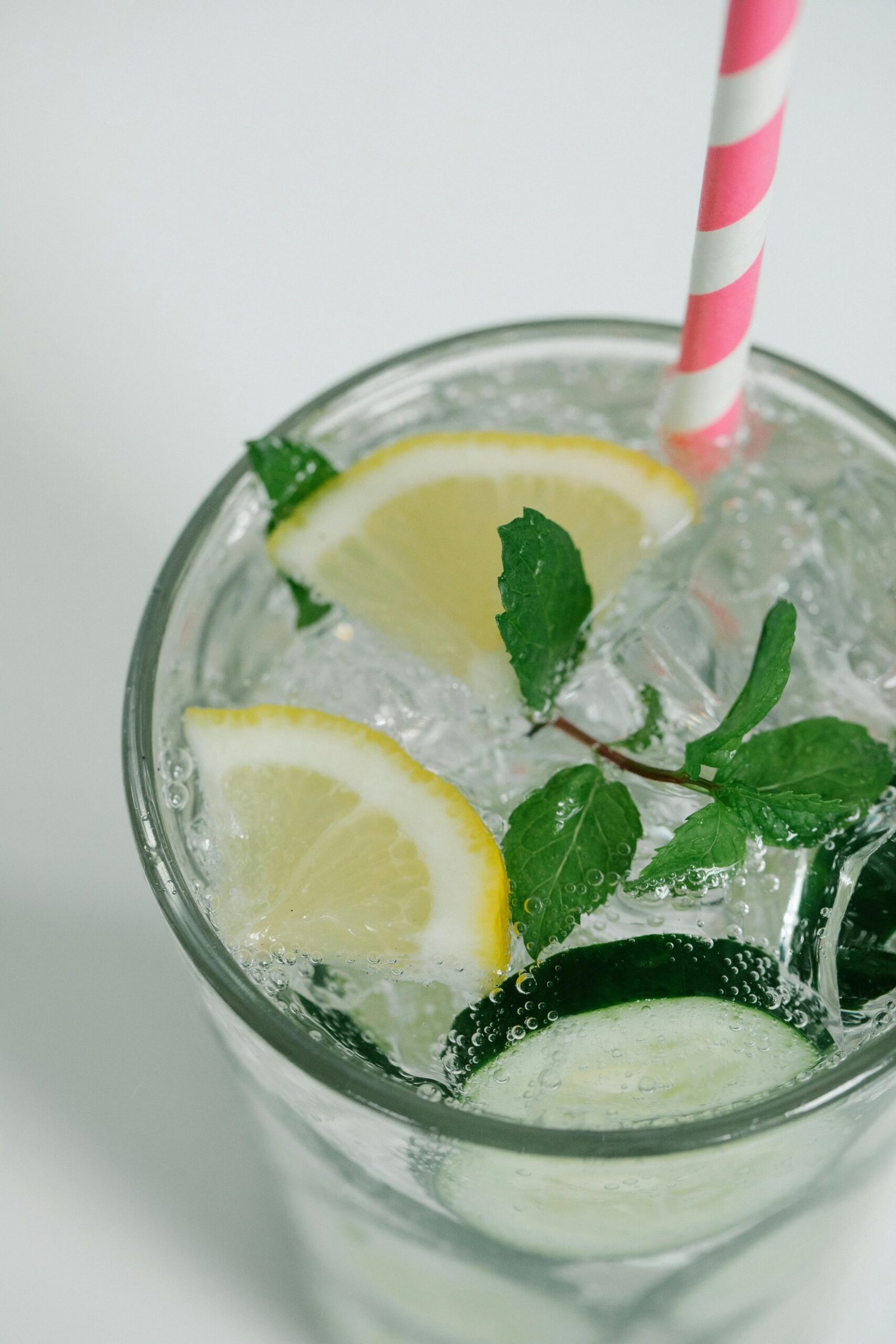 Close-up of a refreshing drink with lemon slices, mint leaves, and a pastel striped straw.